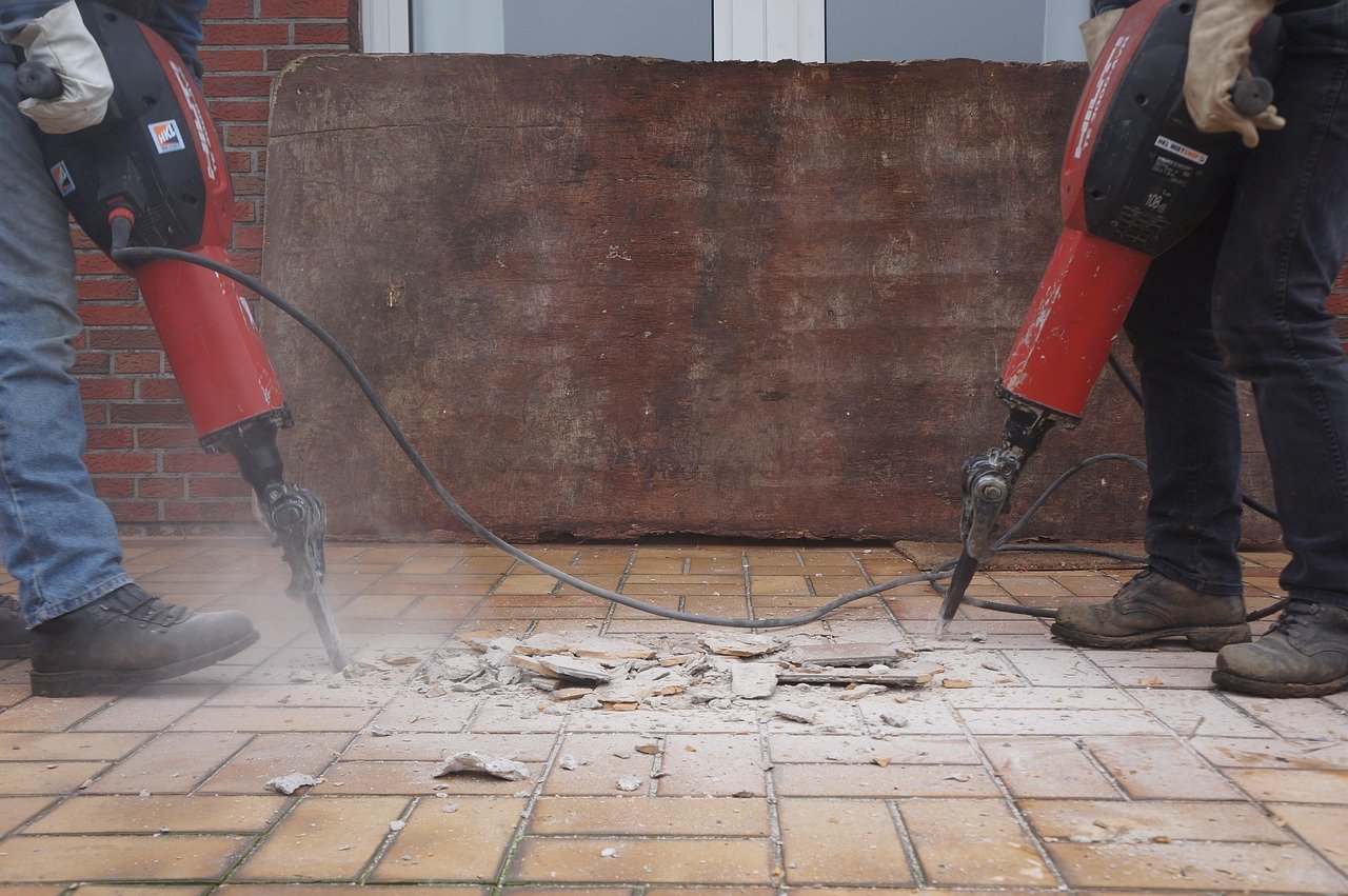 Two workers using pneumatic breakers on a tiled floor