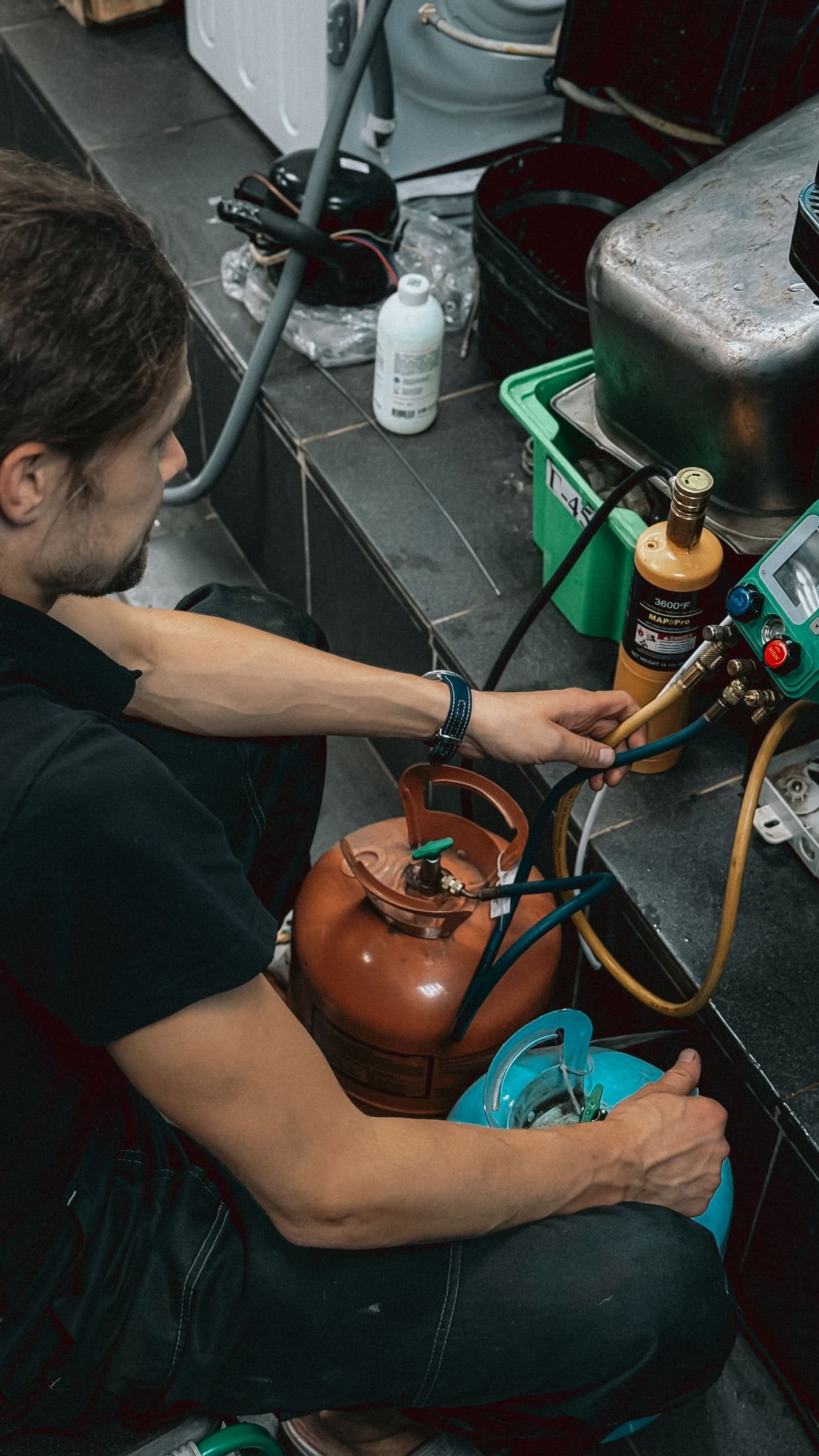 Engineer recovering refrigerant using gauges and a recovery cylinder